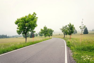 Road by trees on field against clear sky