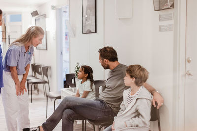 Female doctor talking with girl sitting by family in hospital corridor