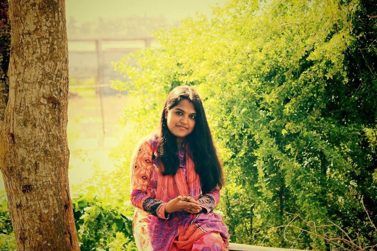 YOUNG WOMAN STANDING BY TREE TRUNK