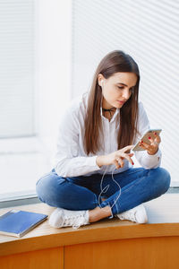 Young woman using smart phone while sitting on table