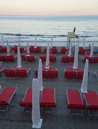 Chairs and tables on beach against sky during sunset