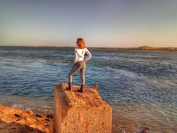 Woman standing on rock at beach against clear sky