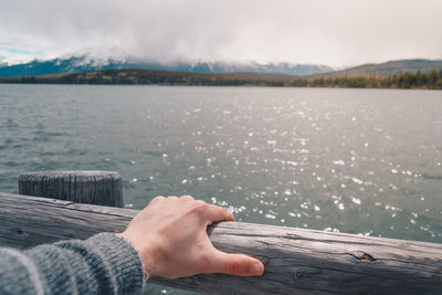 Cropped hand of person on wooden railing against pyramid lake at jasper national park