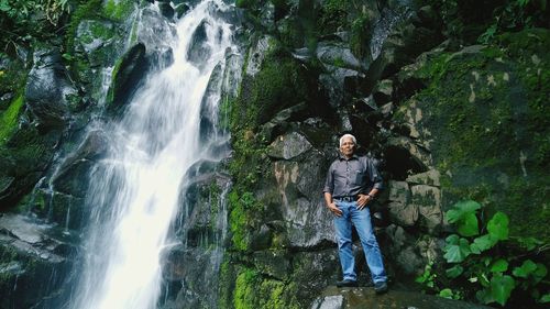 Low angle view of mature man standing on rock by waterfall