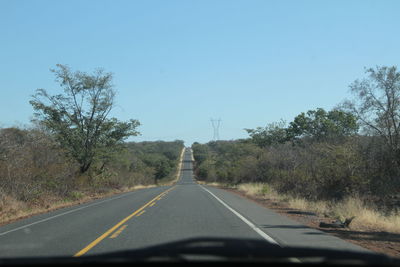 Empty road along trees against clear sky