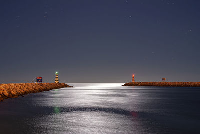 Lighthouse by sea against clear sky at night