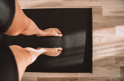 View from above of woman's female legs wearing shorts standing on a black sport mat for yoga fitness