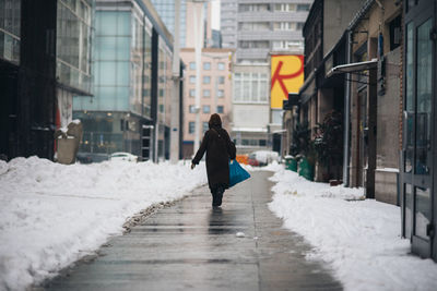 Rear view of woman walking on snow in city