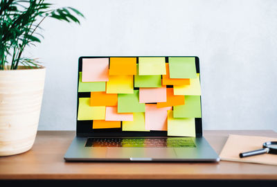 Workplace with laptop computer with many colorful empty sticky notes on display.	