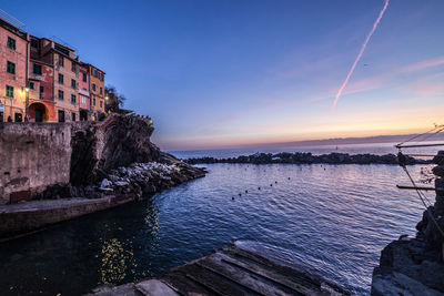 Scenic view of sea by buildings against sky during sunset