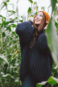 Smiling young woman standing amidst corns on farm