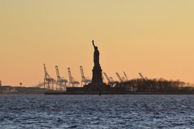 Silhouette statue of liberty in hudson river against clear sky during sunset