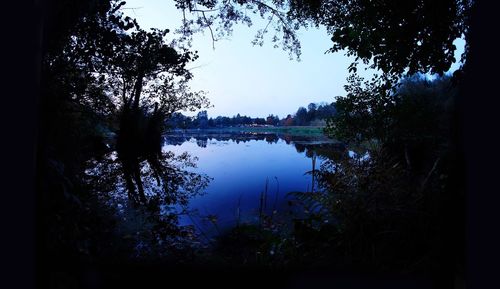 Silhouette trees by lake against sky