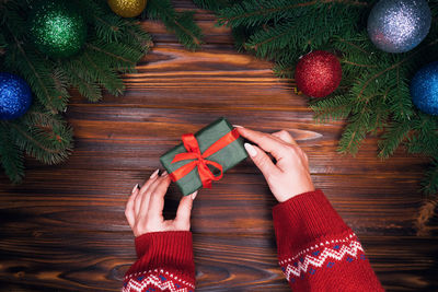 Cropped hands of woman holding wrapped gift over table during christmas