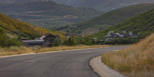 Road amidst field and houses against mountains