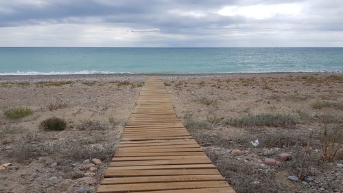 Boardwalk leading towards sea against sky