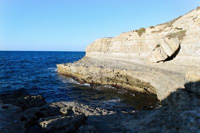 Rock formations by sea against clear blue sky