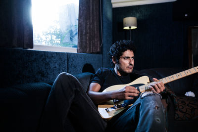 Man playing guitar on sofa at home