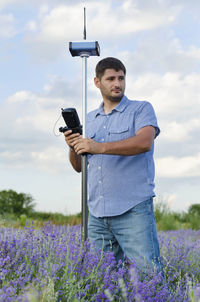 Surveyor using equipment on lavender field against cloudy sky