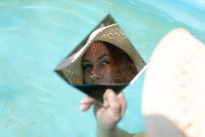 Young woman holding mirror with reflection in wading pool