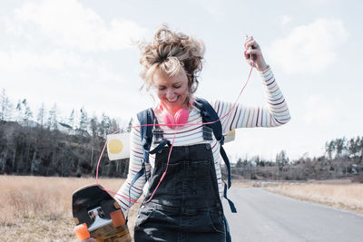 Woman dancing with her skateboard and yoga mat singing whilst outside