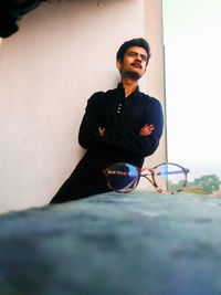 Young man looking away while standing against wall