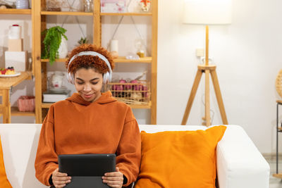 Portrait of young woman using mobile phone while sitting on sofa at home