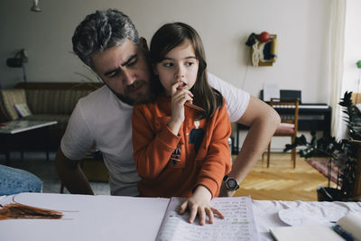 Thoughtful girl doing homework with father at table