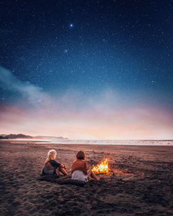 Women sitting by bonfire at beach against sky