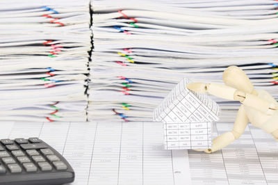 Close-up of wooden figurine holding model house against stacked files