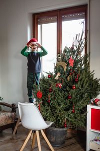 Girl standing on a chair next to christmas tree at home