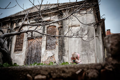 Sad woman covering face with hands by weathered house