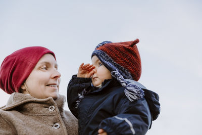 Mother and daughter wearing warm clothing against sky during winter