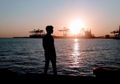 Rear view of man standing at beach against sky during sunset