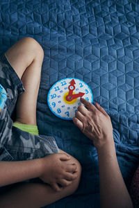 Cropped hand of woman pointing at toy clock by boy on bed