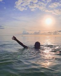 Woman swimming in sea against sky during sunset