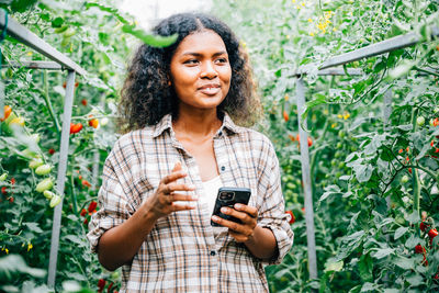 Young woman using mobile phone while standing against plants