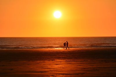 Silhouette people on beach against sky during sunset