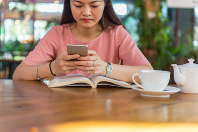 Young woman using mobile phone while sitting on table