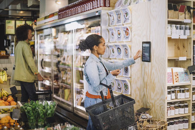 Side view of female customer using digital tablet mounted on wall at grocery store