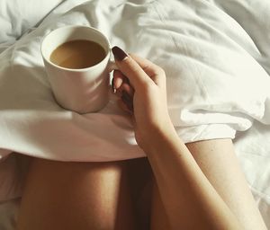 Midsection of woman holding coffee cup on bed