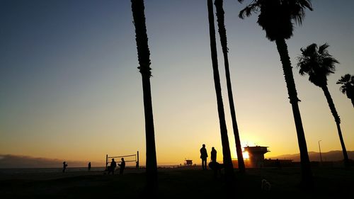 Silhouette people and palm trees at beach against clear sky during sunset