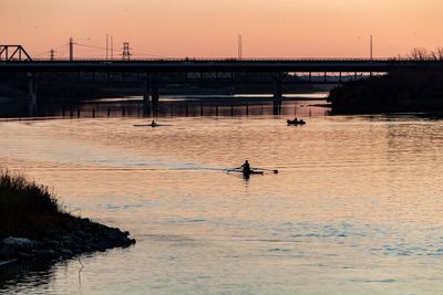 Silhouette man on bridge over river against sky during sunset