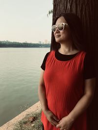 Woman wearing sunglasses while standing by lake against sky