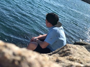 Side view of girl sitting on rock by sea