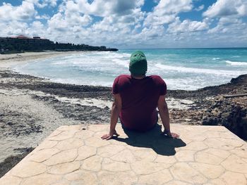 Rear view of man sitting at beach against sky