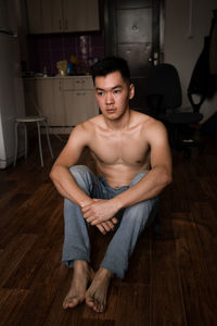 Shirtless young man sitting on hardwood floor
