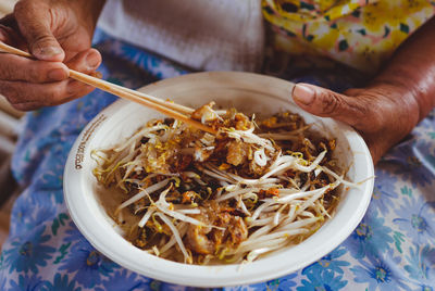 Midsection of person holding noodles in bowl on table