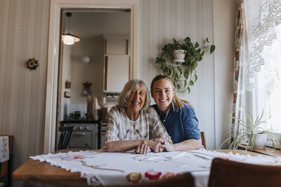 Portrait of happy female caregiver with senior woman sitting at home