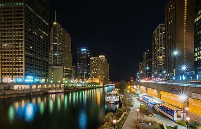 Boats moored in chicago river amidst illuminated buildings in city at night